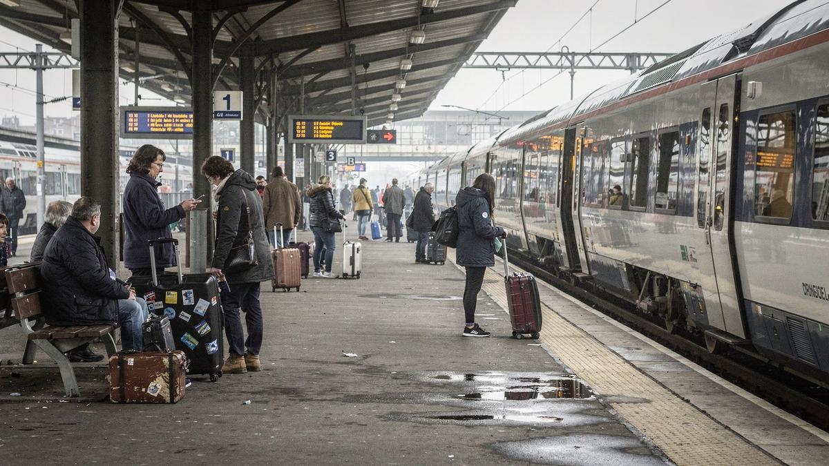 Group of travellers with suitcases waiting on a station platform beside a long-distance train
